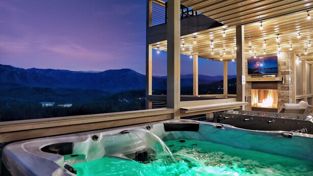 Un jacuzzi con vistas a la montaña, chimenea y televisor en un entorno moderno al aire libre.