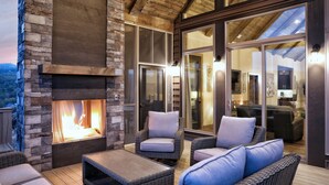 Un área de estar al aire libre con mobiliario de mimbre, una chimenea y vistas del interior a través de puertas de cristal.