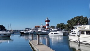 Un puerto deportivo con varios yates amarrados, un faro destacado y un cielo azul despejado.