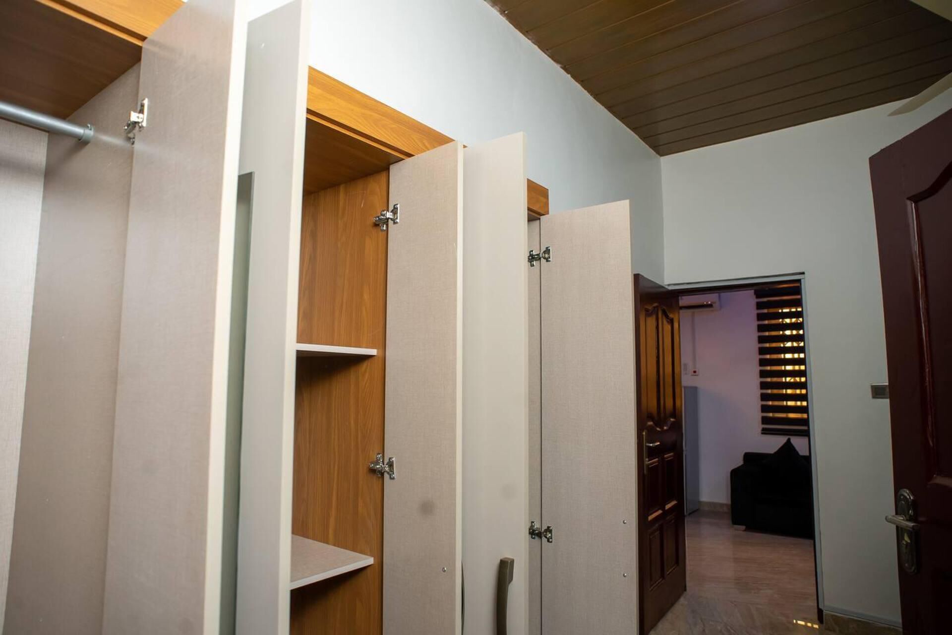 A hallway with a wooden door, a wardrobe with a mirror, and a black sofa in the background.