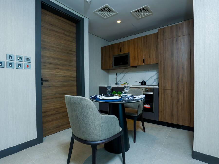 A modern kitchen with wooden cabinets, a dining table set for two, and a microwave above it.