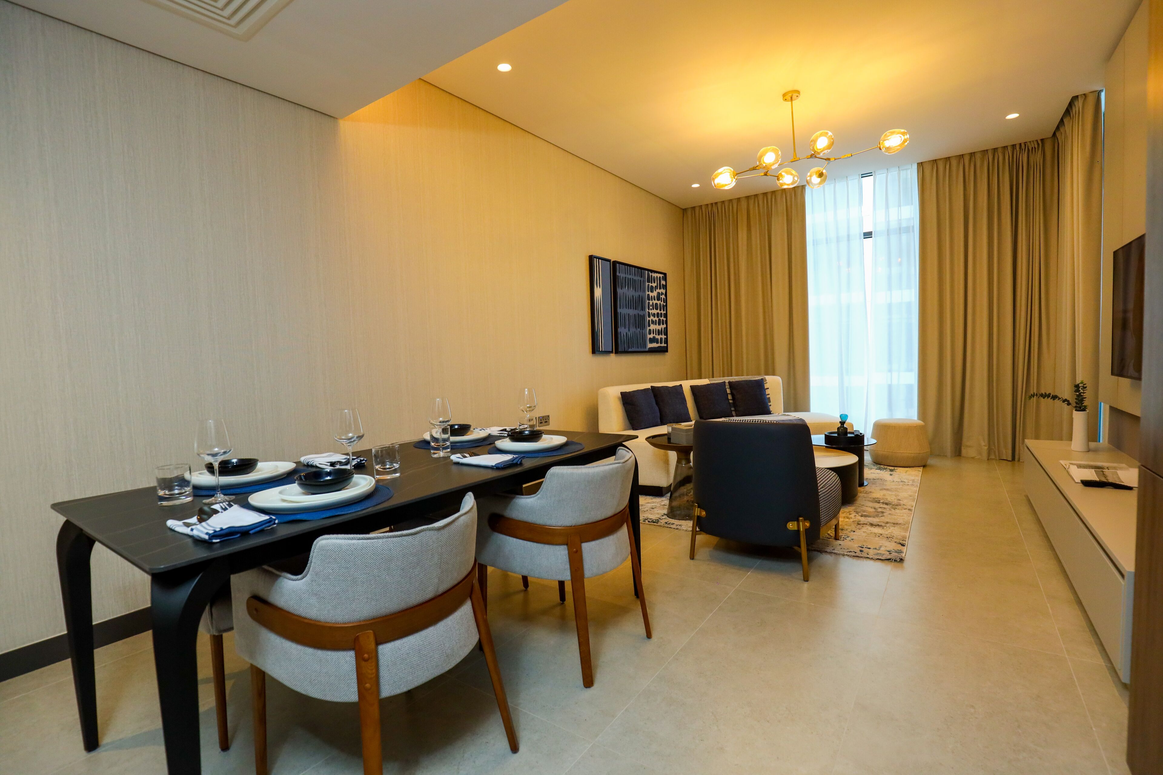 Una sala de estar moderna con comedor, que incluye un sofá, sillas, una mesa de centro y una mesa de comedor preparada para cuatro personas.