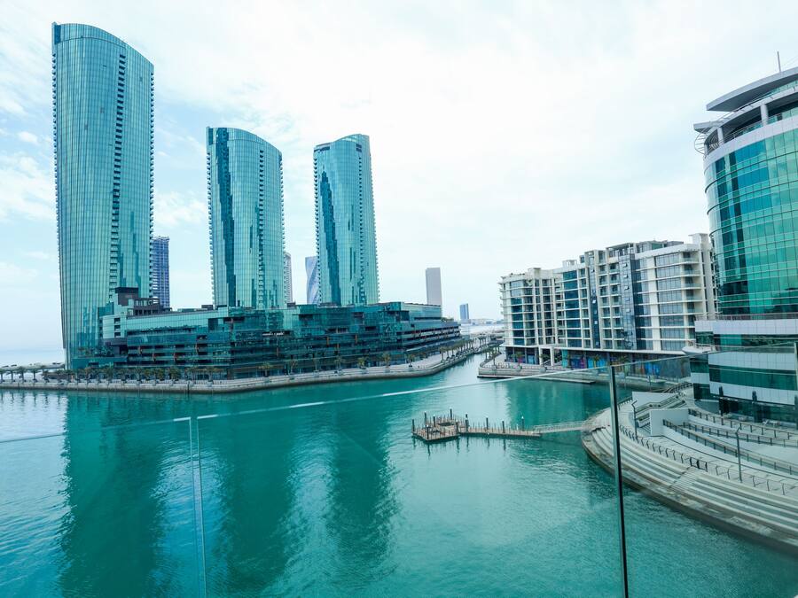 Vista al agua de modernos edificios altos, un puerto deportivo y un paseo peatonal.
