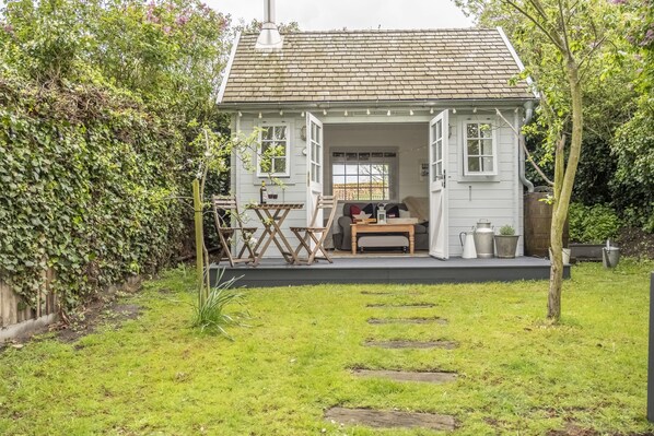 Une petite maison blanche avec un toit en tuiles, une terrasse en bois et un jardin agrémenté de pierres plates servant de pas.