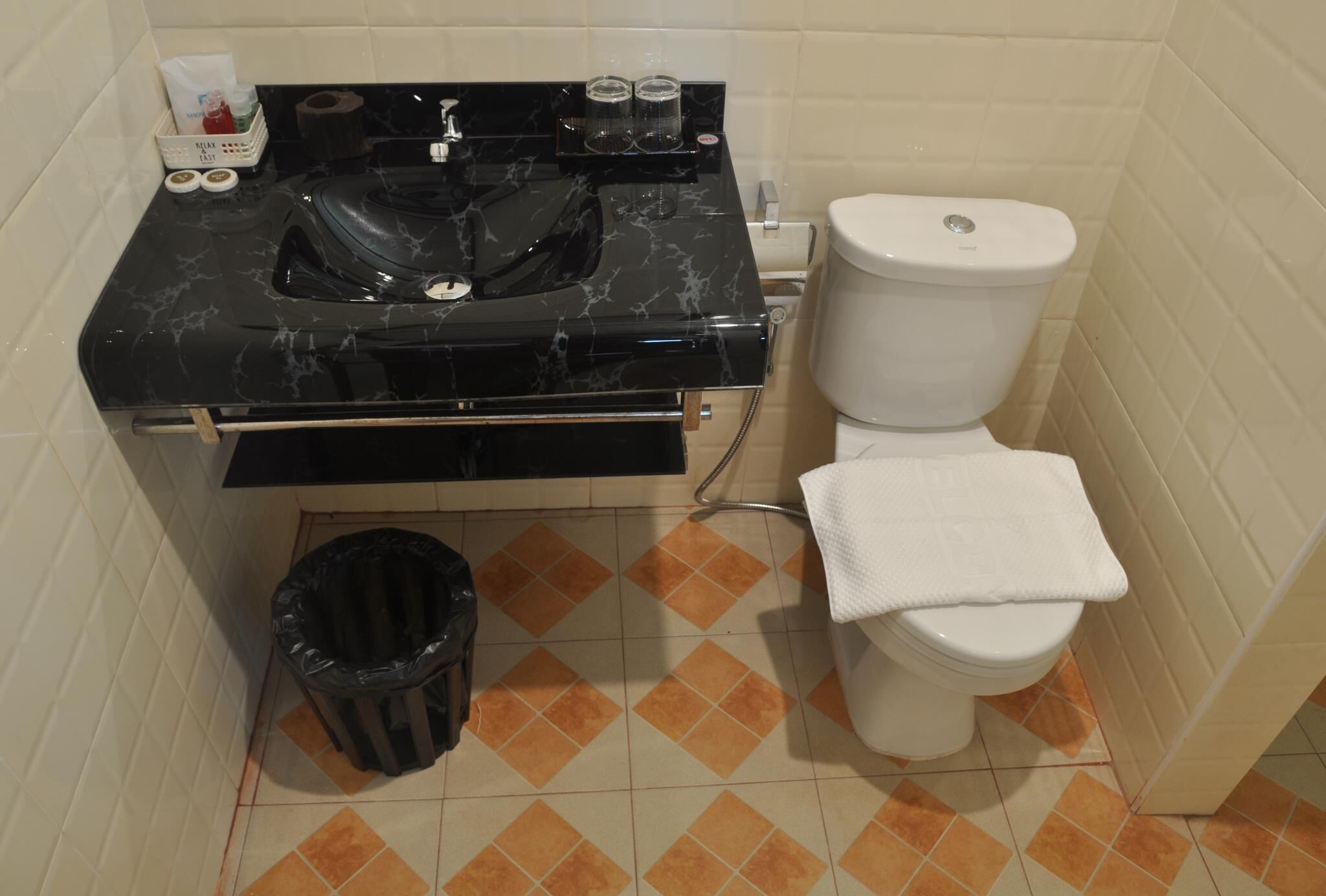 A bathroom with a black marble sink, white toilet, and a trash bin.