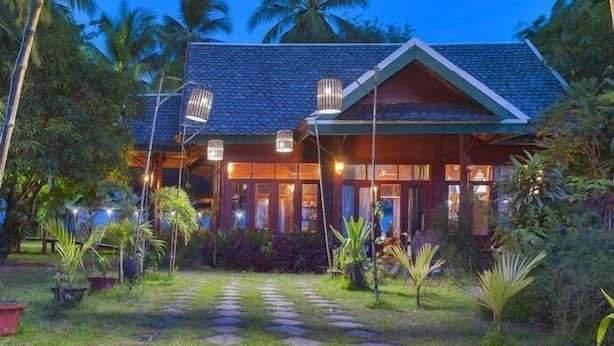 A two-story building with a tiled roof and a covered porch. There are two large, cylindrical, hanging lights above the porch. - Jenda the views (Champasak)