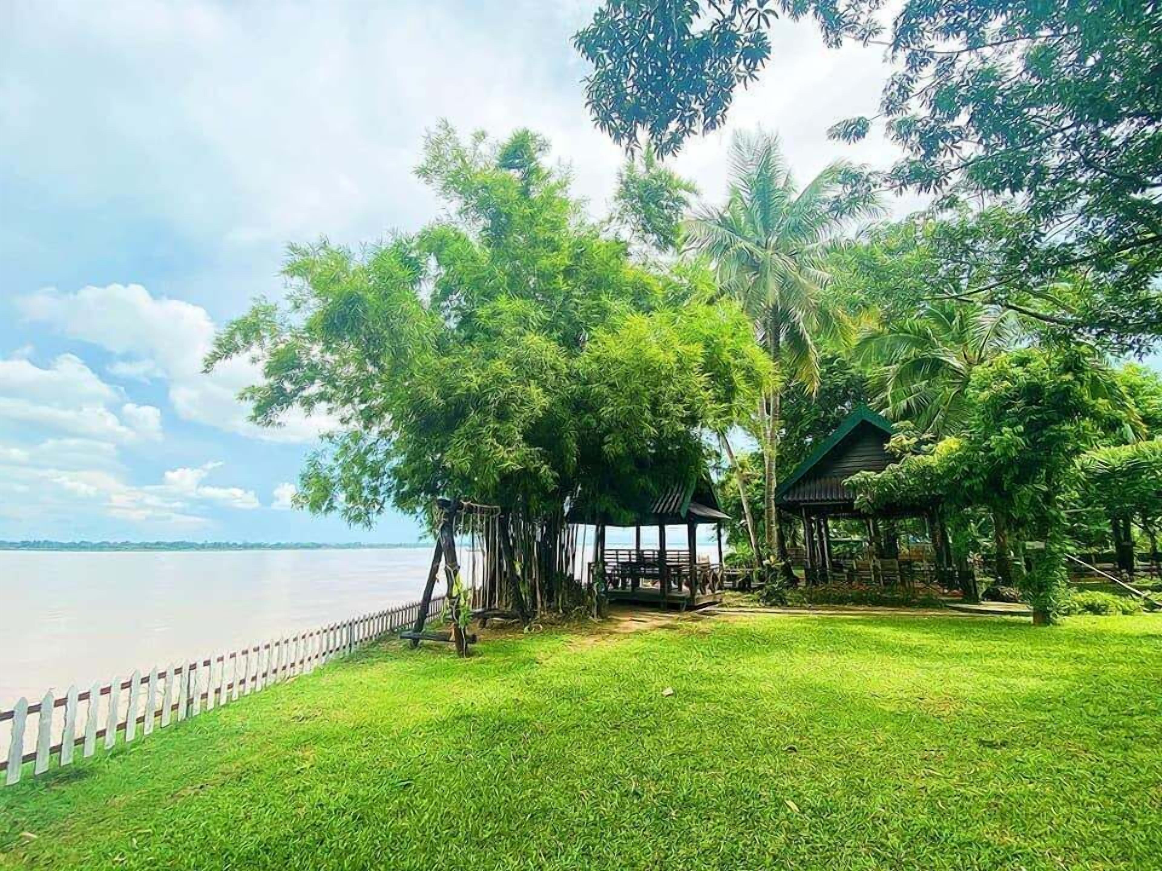 A grassy area with a wooden fence, a small pavilion, and trees.