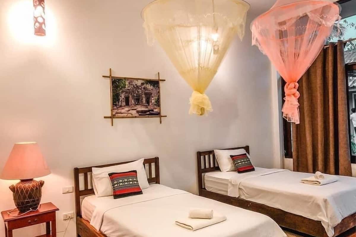 A hotel room with two beds, a bedside lamp, a wall-mounted picture, and a hanging mosquito net.