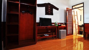 A room with a wooden wardrobe, a desk with a computer, a small fridge, and a sliding door closet. - Jenda the views (Champasak)