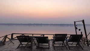 A wooden deck with three lounge chairs facing a calm lake at sunset. - Jenda the views (Champasak)