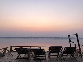 Una terraza de madera con tres sillones de relax mirando a un lago tranquilo al atardecer.
