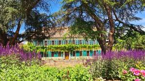 A building with a stone facade, green shutters, and a garden with purple flowers. - Ritterhof guest rooms at the Fitz-Ritter winery - VDP/Organic (Bad Dürkheim)