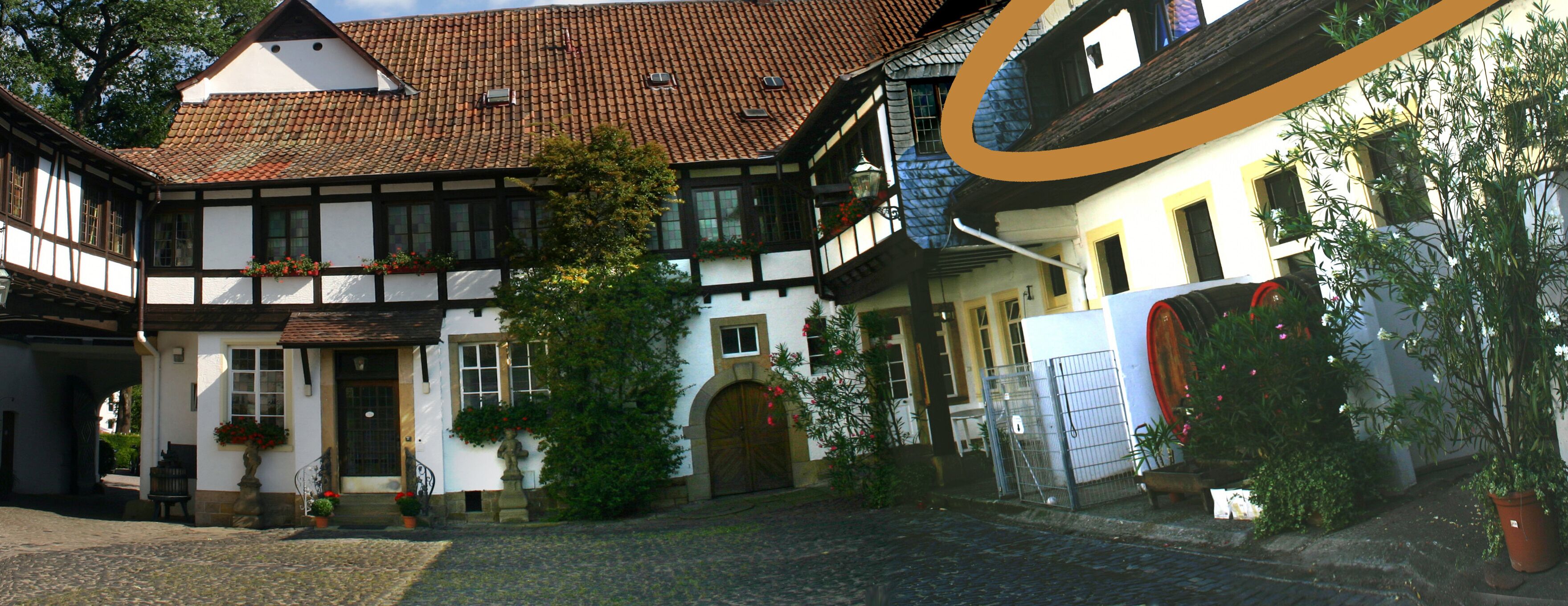 A traditional European courtyard with a cobblestone path, a wooden door, and a white building with a tiled roof.