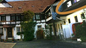 A traditional European courtyard with a cobblestone path, a wooden door, and a white building with a tiled roof.