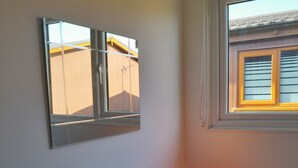 A corner room with a wooden cabinet, a wall-mounted mirror, and a window with blinds. - Perfect Chalet to Relax in k4 (Mablethorpe)