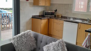 A modern kitchen with wooden cabinets, a microwave, and a dishwasher. There is a grey sofa with fluffy cushions in the living area. - Perfect Chalet to Relax in k4 (Mablethorpe)