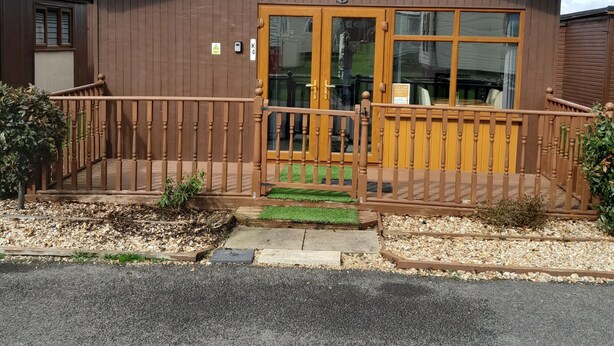 A two-story building with a brown exterior, a green entrance mat, and a wooden fence. - Perfect Chalet to Relax in k4 (Mablethorpe)