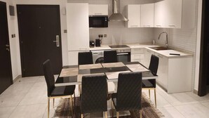 A modern kitchen with white cabinetry, a central island, and a dining area with a black and white table and chairs. - Luxurious & Comfy Gem-5 Star Location-pools, Gym! (Accra)