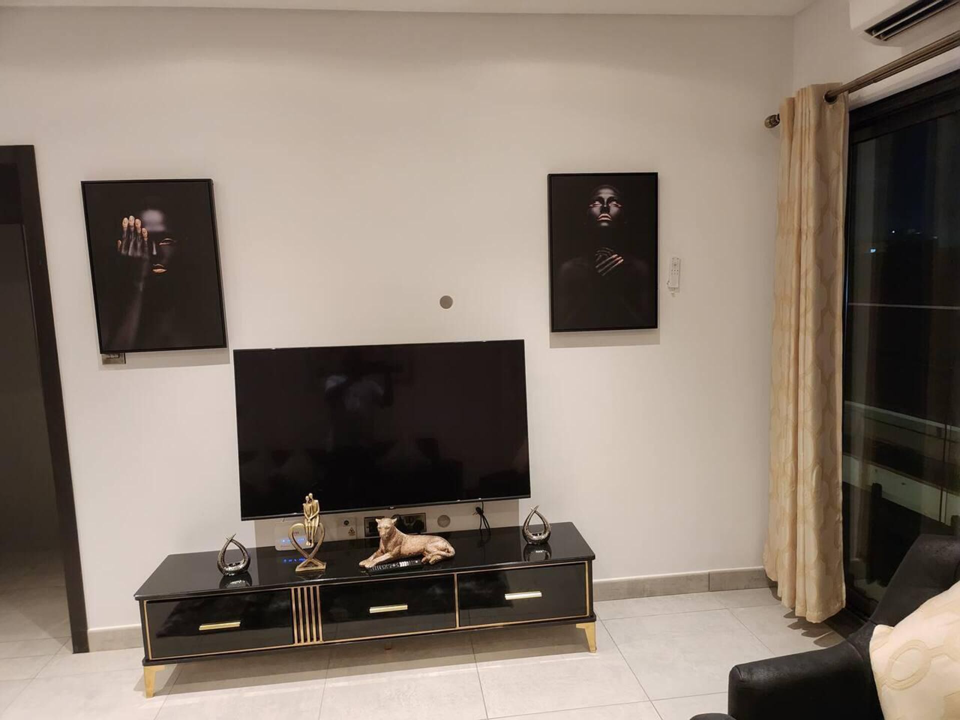 A modern living room with a large flat-screen TV, a black entertainment unit with decorative items, and two framed artworks on the wall.