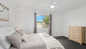 A bedroom with a bed, a dresser, a ceiling fan, and a window with curtains. - Beach Shack 5 (Crescent Head)