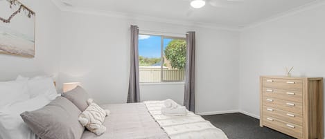 Une chambre à coucher avec un lit, une commode, un ventilateur de plafond et une fenêtre avec des rideaux.