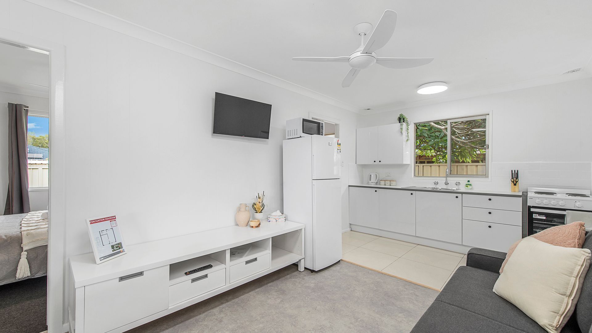 A modern kitchen with white cabinets, a microwave, and a stove. There is a ceiling fan and a window with a view of greenery outside.