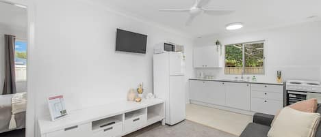 A modern kitchen with white cabinets, a microwave, and a stove. There is a ceiling fan and a window with a view of greenery outside.
