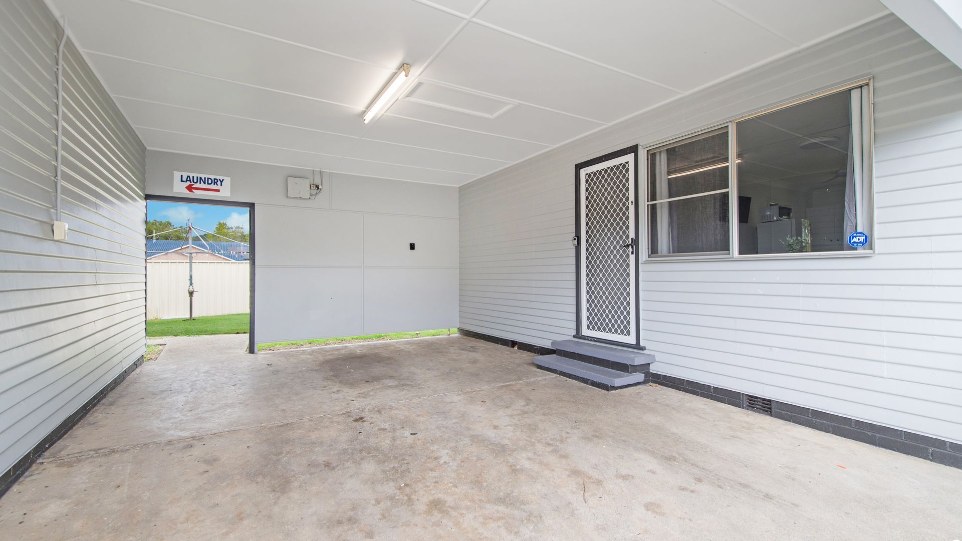A clean, empty hallway with a laundry sign, a door with a security screen, and a window with a view of the outside.