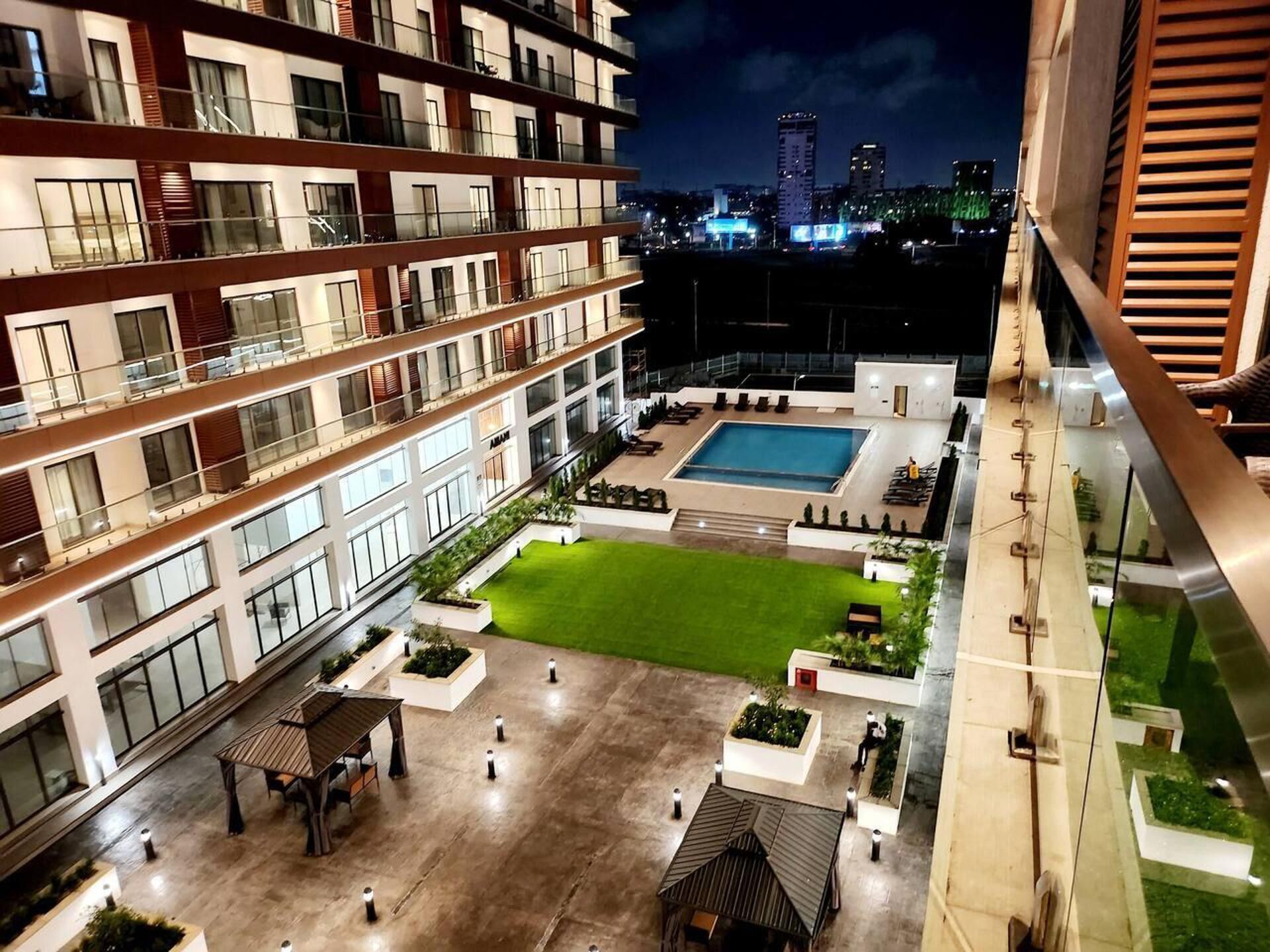A multi-story hotel with a rooftop pool, outdoor seating, and a well-maintained lawn.