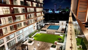 Un hotel de varios pisos con piscina en la azotea, mobiliario exterior y un césped bien cuidado.