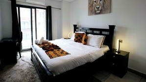 Habitación de hotel con una cama grande, un escritorio, una silla, un cuadro y una ventana con cortinas.