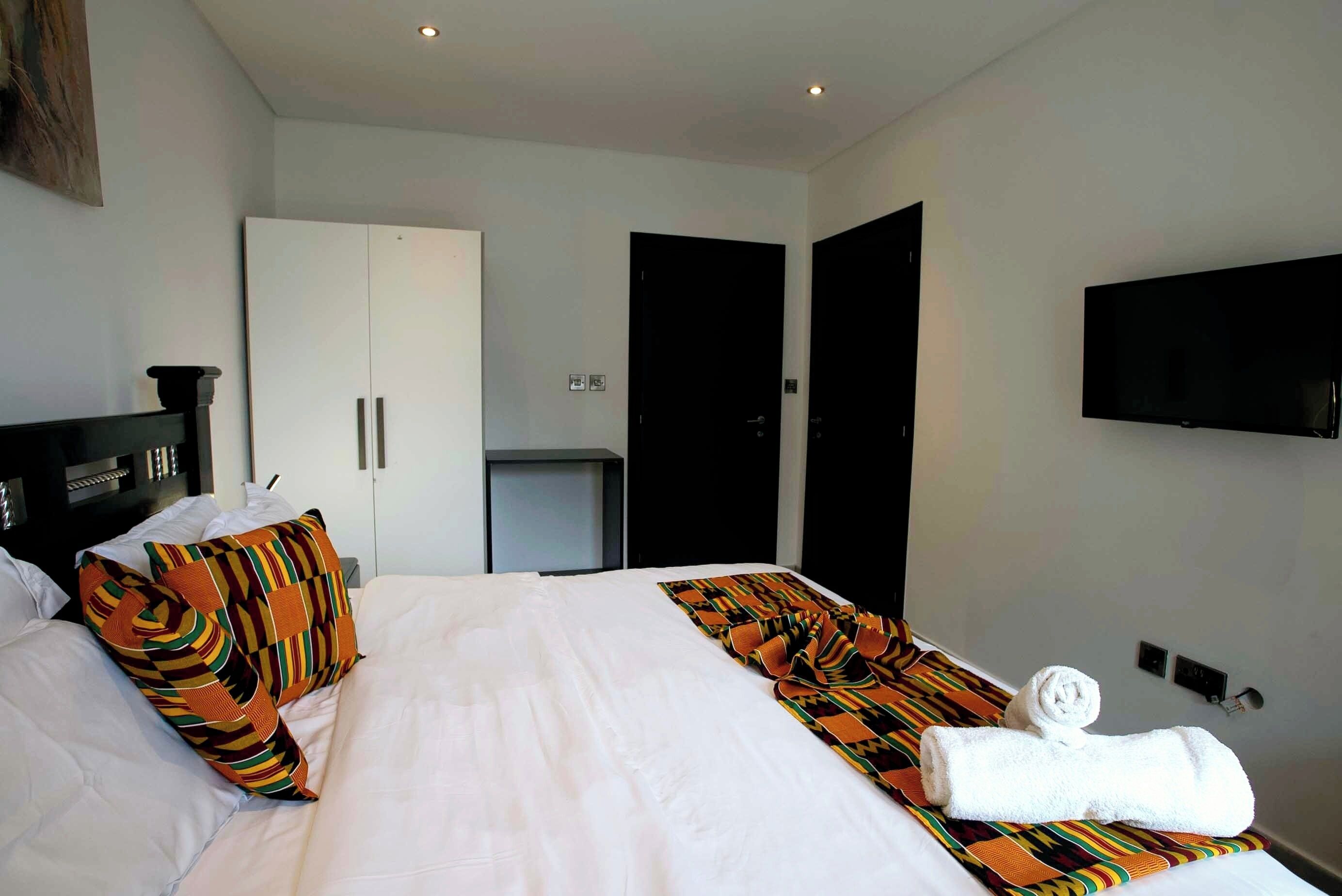 A hotel room with a large bed, a wardrobe, a television, and a small desk.