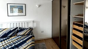 Ein Schlafzimmer mit einem Bett, einem grauen Teppich, einem gerahmten Bild an der Wand und einer Schiebetür zum Kleiderschrank.
