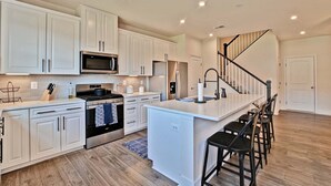 A modern kitchen with white cabinetry, stainless steel appliances, and a central island with bar stools.