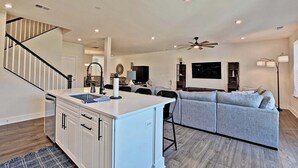 A modern kitchen with a central island, a dining area with a gray sofa, and a staircase leading to an upper level.