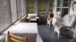 A sunroom with a table and chairs, large windows, and a view of greenery outside.