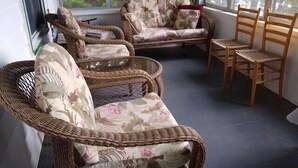 A cozy corner with wicker chairs and a sofa, large windows, and a view of trees.