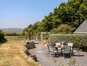 A patio with a table and chairs, surrounded by a stone wall and a variety of plants.
