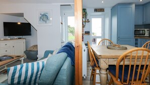 Uma sala de estar aconchegante com um sofá, uma televisão e um espaço de jantar com cadeiras de madeira e uma mesa.