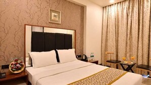 A hotel room with a large bed, a nightstand, a small table, and a ceiling fan. - Apricsu Treeo Lonavala (Mawal)