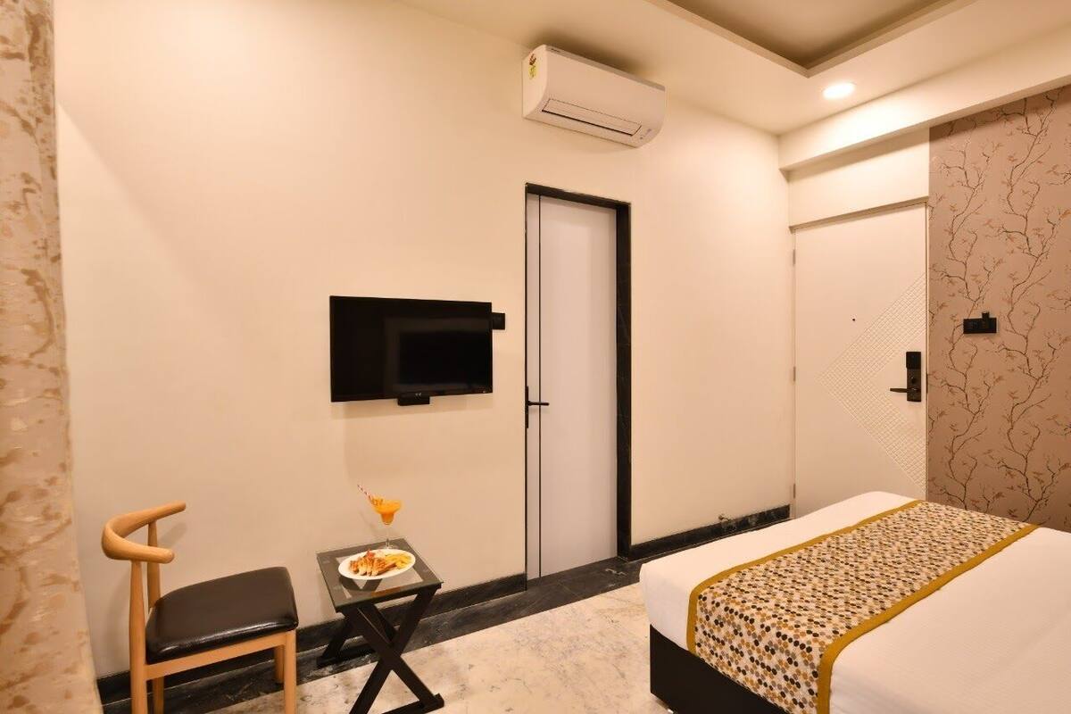 Una habitación de hotel con una cama, un televisor montado en la pared, una mesita con un plato de comida y una silla.