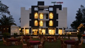 A modern building with multiple balconies and large windows, surrounded by outdoor seating areas with round tables and chairs. - Apricsu Treeo Lonavala (Mawal)