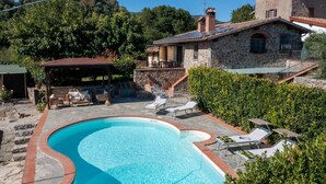 A swimming pool with lounge chairs, a stone house, and a covered patio area.