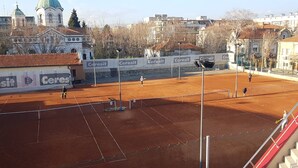 A tennis court with a net, surrounded by buildings and advertisements.