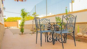 Een terras met een metalen tafel en stoelen, een bloempot en een stenen muur.
