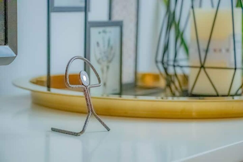 A metal sculpture on a white surface with a yellow base, surrounded by framed artwork and a candle holder.