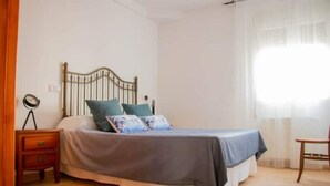 Een slaapkamer met een bed, een nachtkastje, een stoel en een raam met gordijnen.