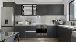 A modern kitchen with dark cabinetry, stainless steel appliances, and a glass dining table. - The Signature 307 (Cape Town)