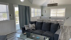 Un salon moderne avec un canapé gris, une table basse en verre et un coin repas doté de meubles blancs.