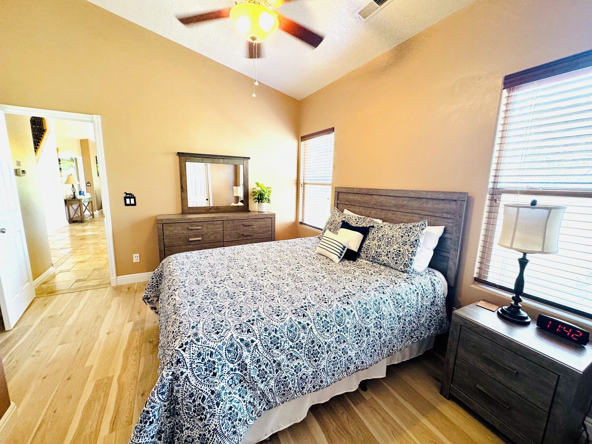 A bedroom with a bed, a nightstand, a dresser, a ceiling fan, and a window with blinds.